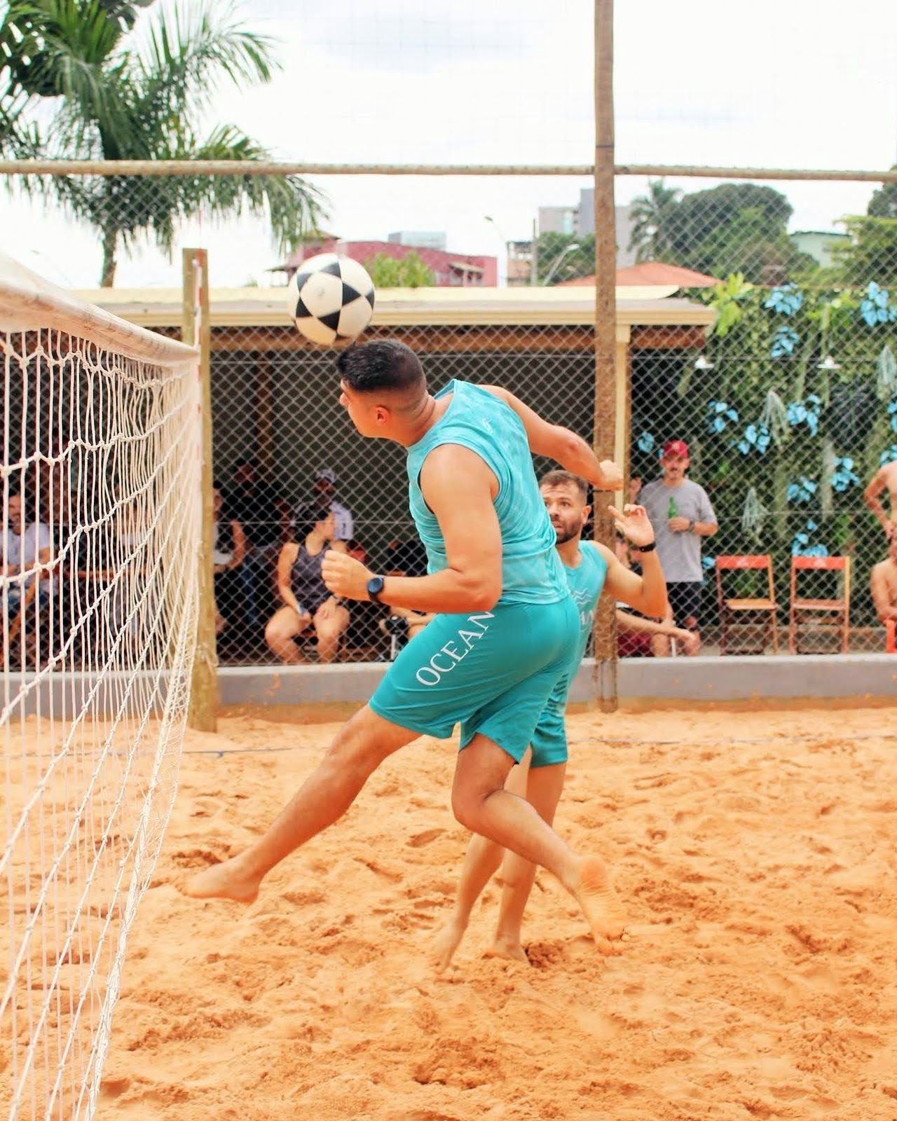 Jogadores de futevôlei com uniforme turquesa da Ocean numa quadra de areia